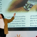 Photo of David Berman on stage pointing to an image of a cell phone designed to dim the portions of the screen that don't currently have focus.