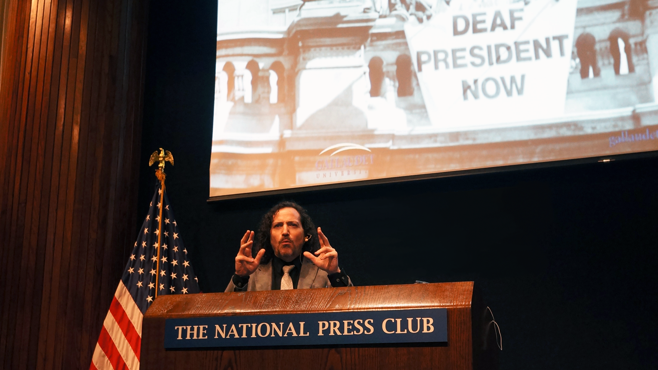 David in Washington giving talk and gesturing behind the National Press Club podium