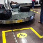 Image of an accessibility sign on the floor near the luggage carousel marking a reserved space for accessibility. 